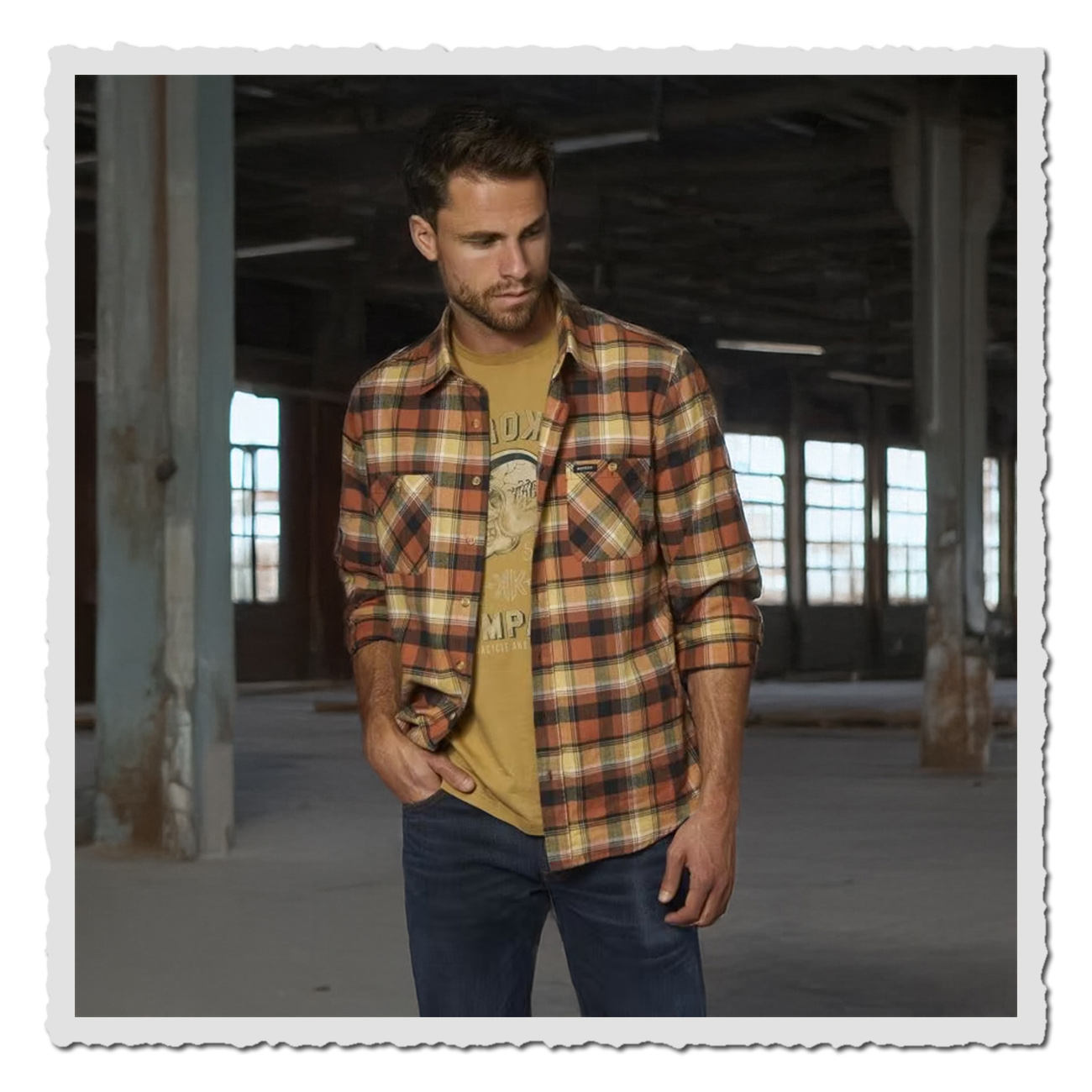 Mann trägt The Rokker Company Flanellhemd Freemont in Gelb-Rot-Karo mit T-Shirt und Jeans in einer alten Fabrikhalle